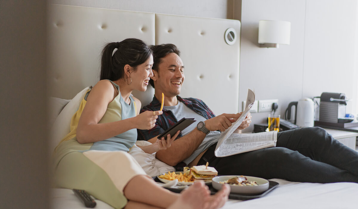 Couple smiling laying in bed enjoying room service.